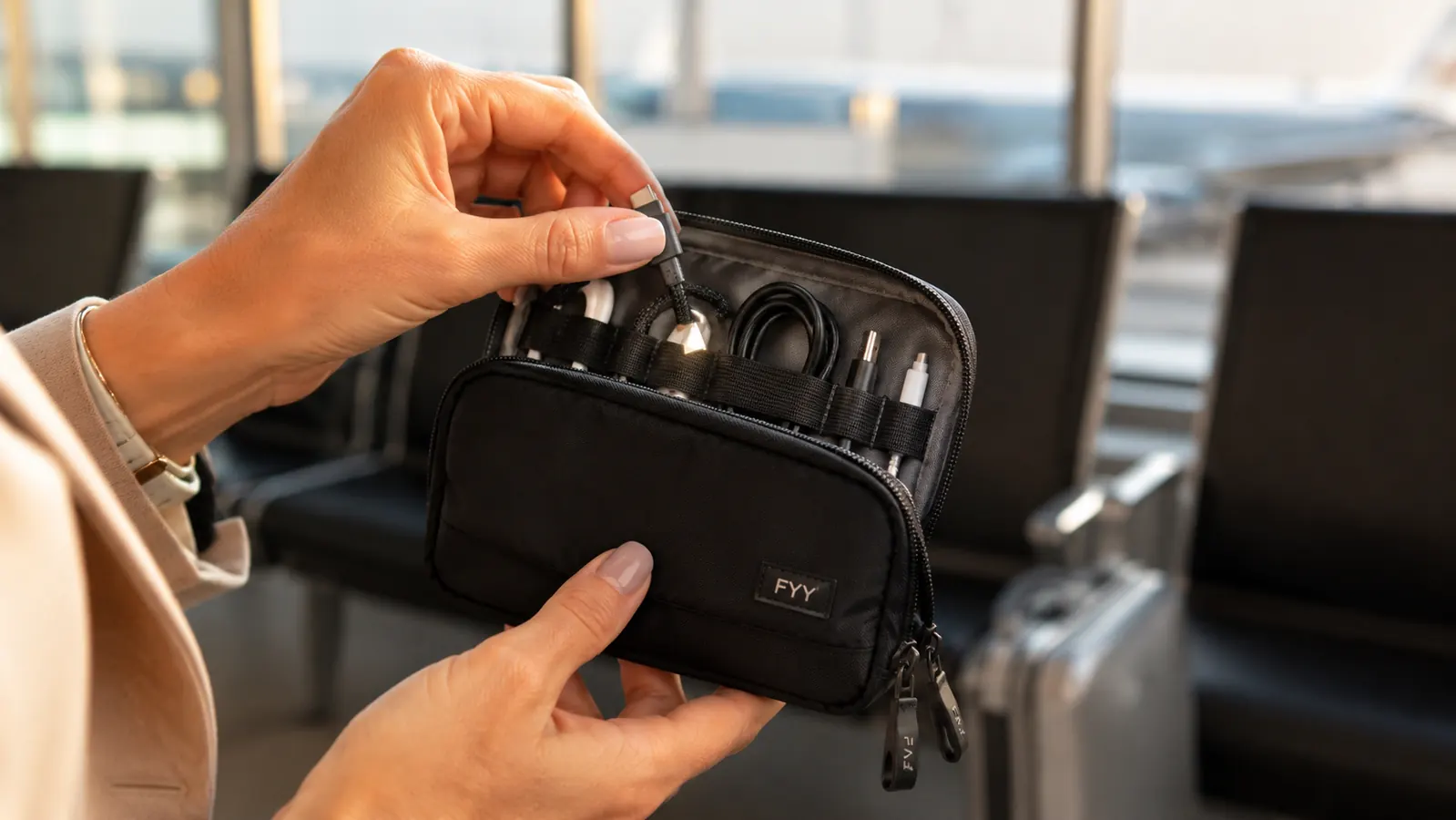 Traveler holding the FYY cable organizer open in one hand while reaching for a USB cable with the other hand in an airport terminal
