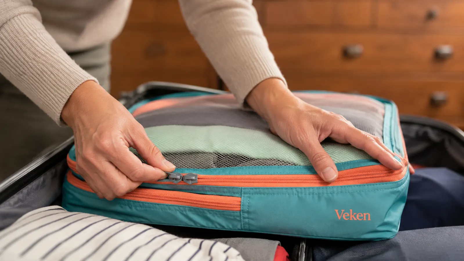Hands pressing down the compression zipper on a Veken packing cube filled with folded shirts