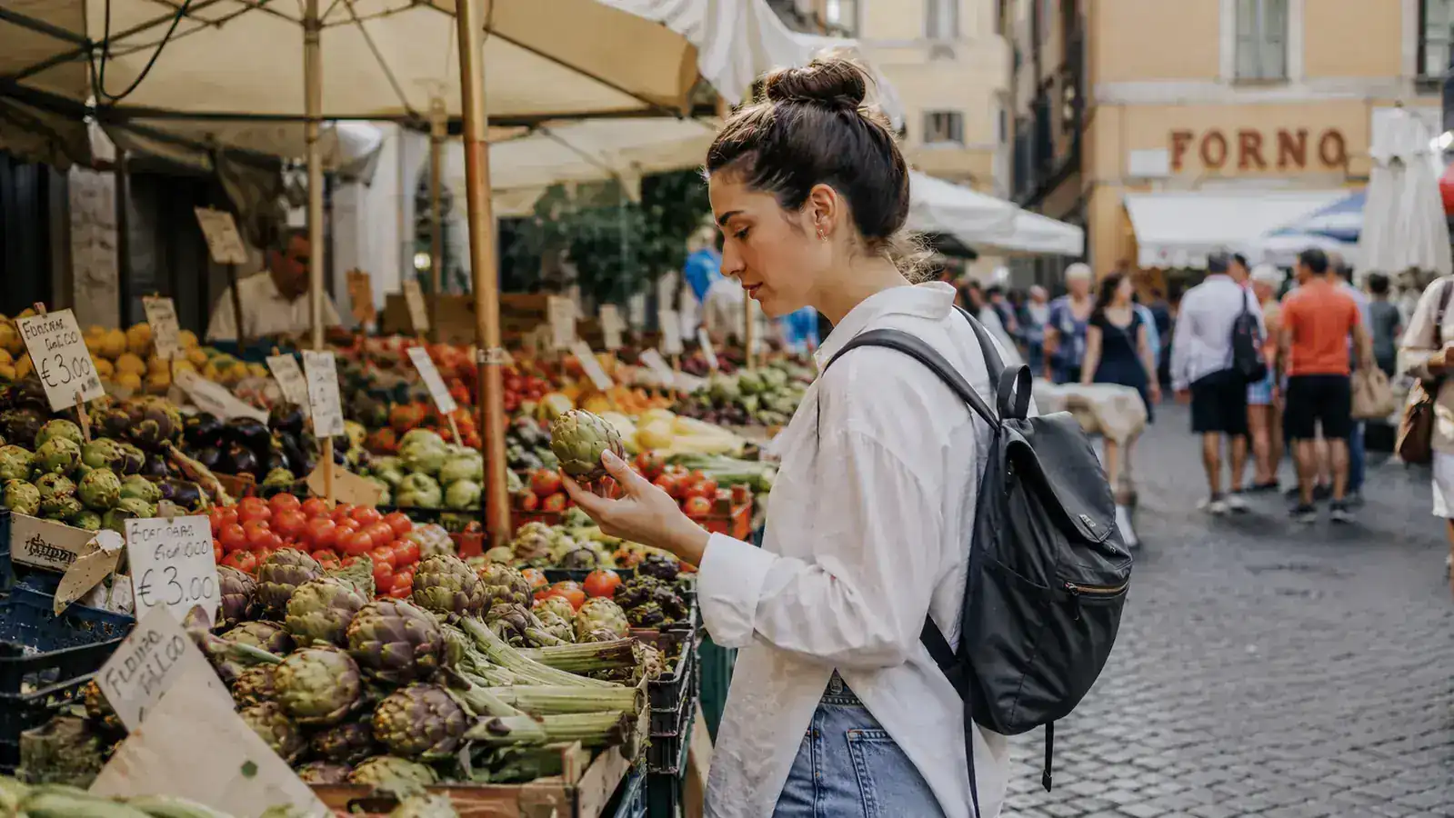 Woman at a Roman market with a small backpack, browsing fresh produce stalls